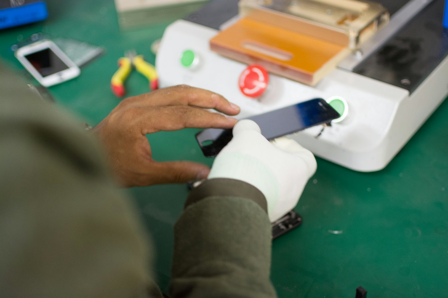 Tecnico che ripara uno smartphone su un banco da lavoro verde.