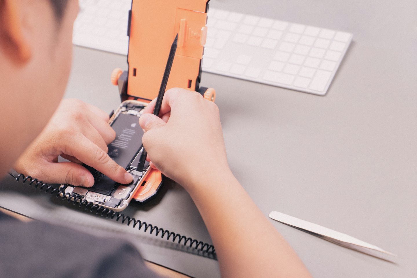 Mani di tecnico che riparano uno smartphone aperto con attrezzi.