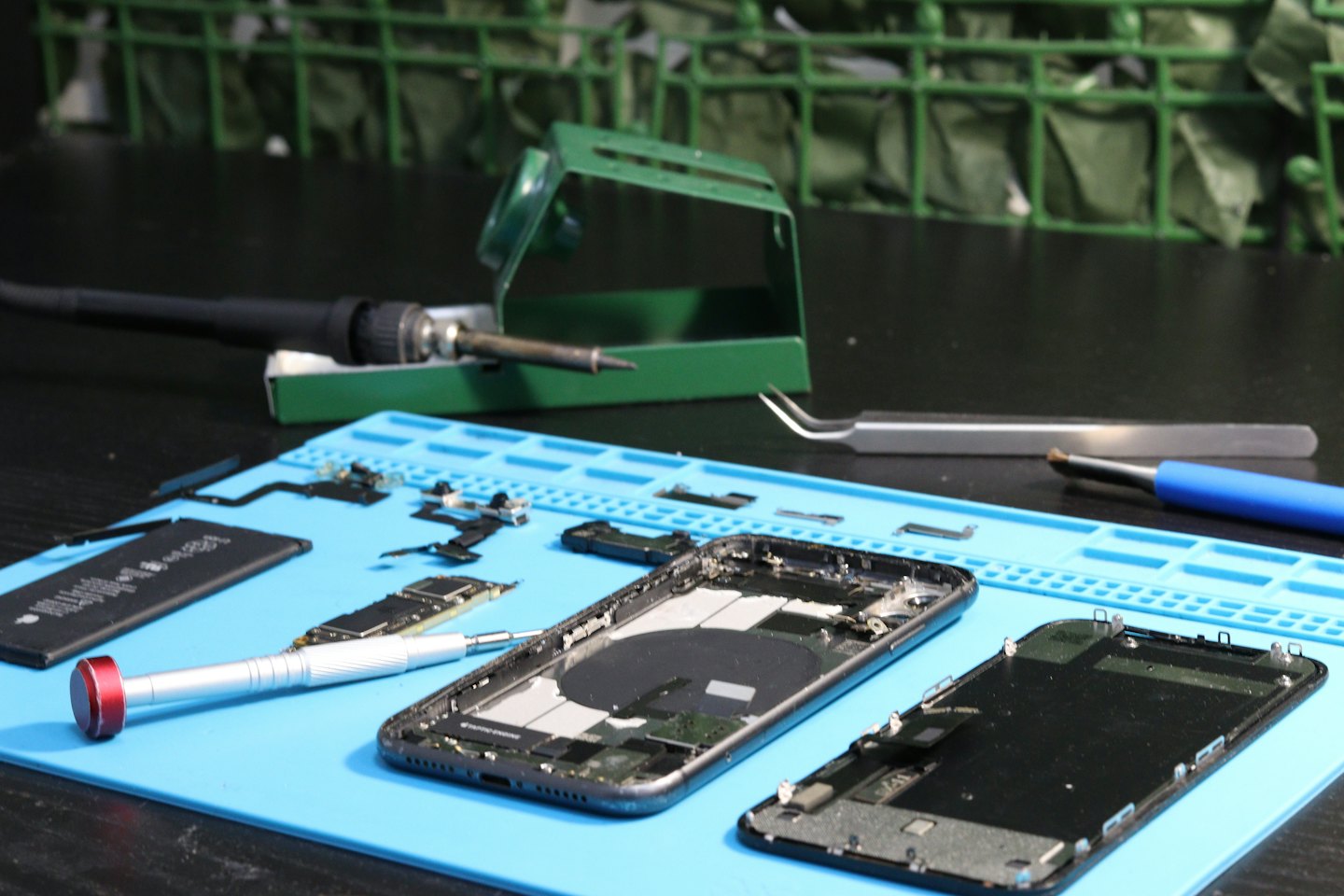 Componenti di smartphone smontati disposti su un tappetino blu per riparazioni.