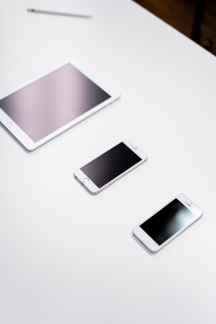 Overhead view of a digital tablet, smartphone, and stylus on a white surface.
